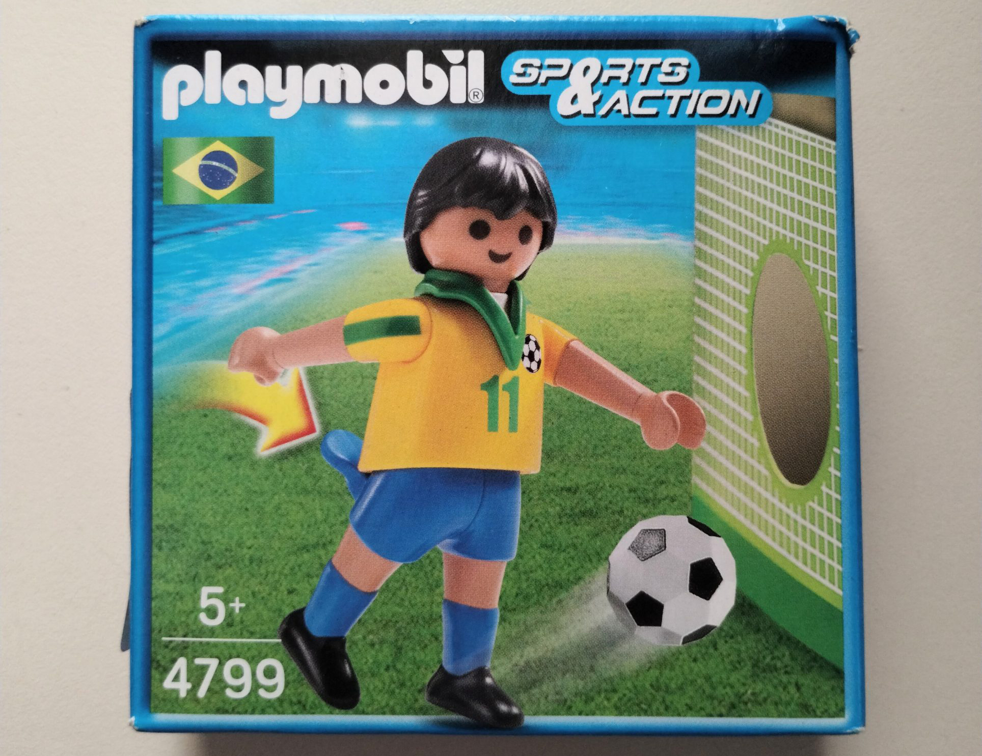 Boneco em plástico com roupa da seleção brasileira de futebol, camisa 11, na embalagem original de papelão lacrada, 2014. Coleção do Museu Histórico Nacional do Rio de Janeiro